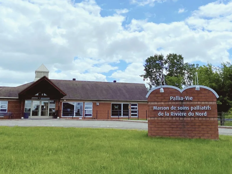 The Pallia-Vie palliative care home in Saint-Jérôme, a low brick building behind its sign, under a summer sky