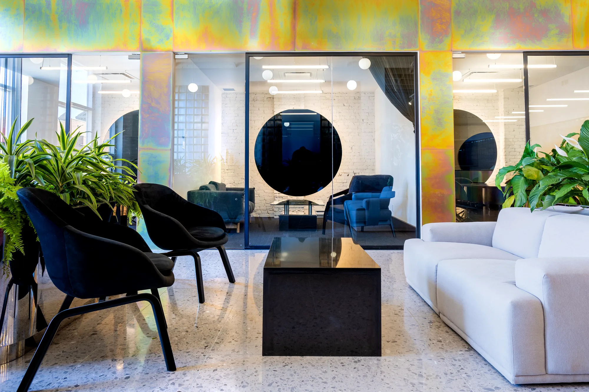Spacial's lounge: white sofas, black chairs and glass meeting rooms under an iridescent zinc beam