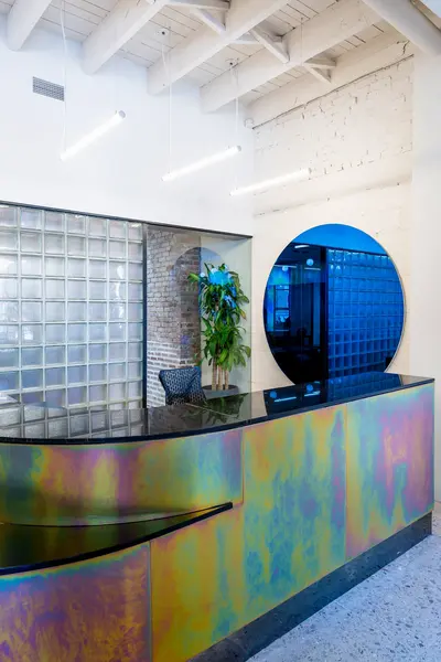 Reception desk in iridescent zinc beside a wall of glass blocks