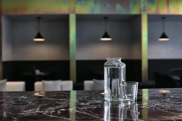 A carafe on the marble counter, booths under iridescent beams behind